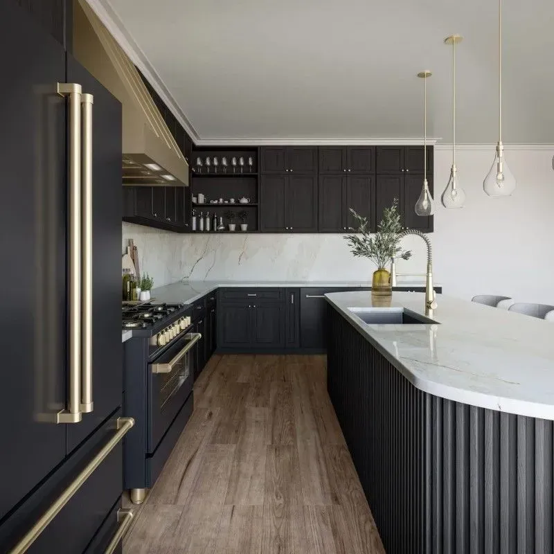 Black kitchen with gold hardware, marble countertops, and light wood floors.