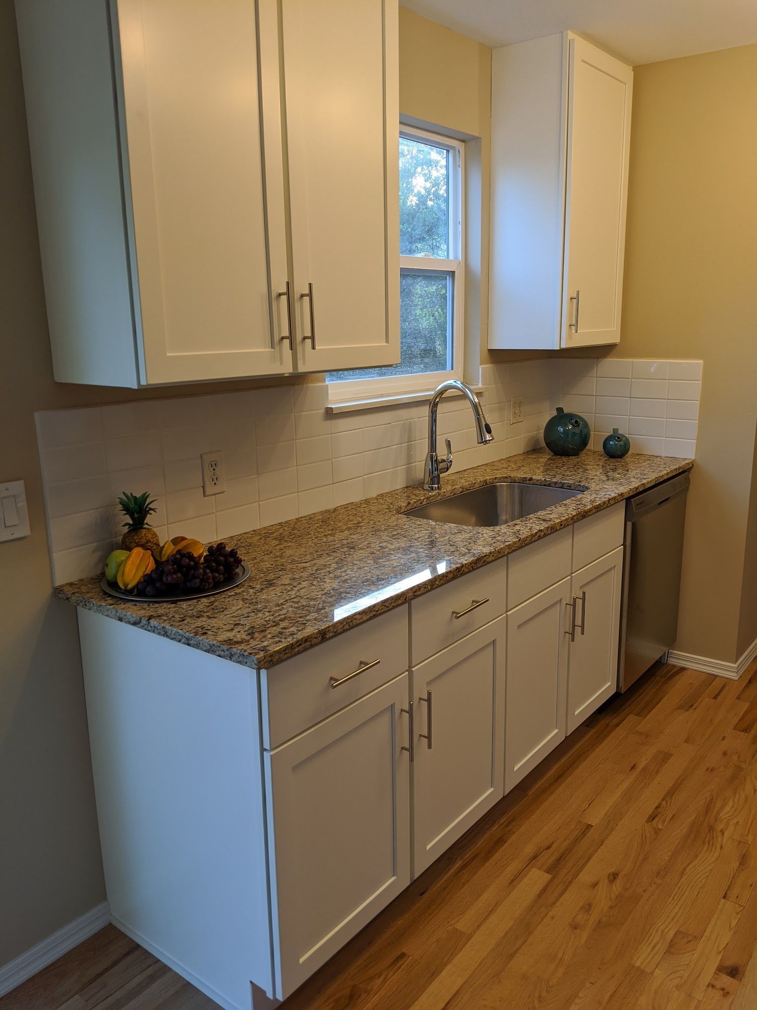 White kitchen cabinets with granite countertop and stainless steel sink.