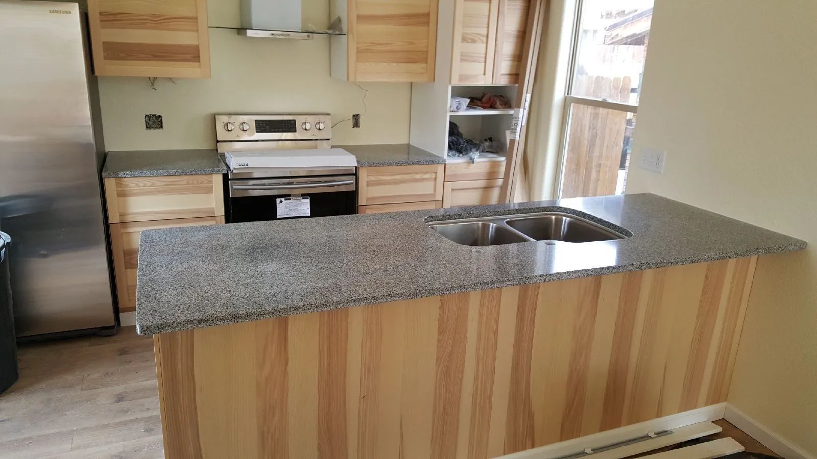 Kitchen with light wood cabinets, granite countertops, stainless steel appliances, and a kitchen island with a sink.