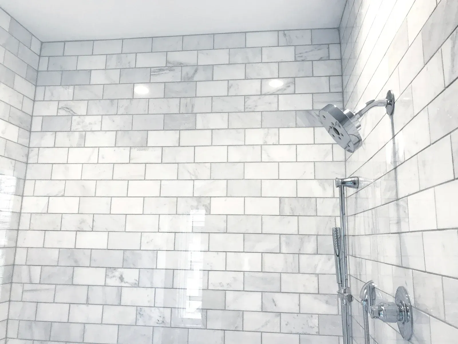 White tiled shower with silver fixtures.