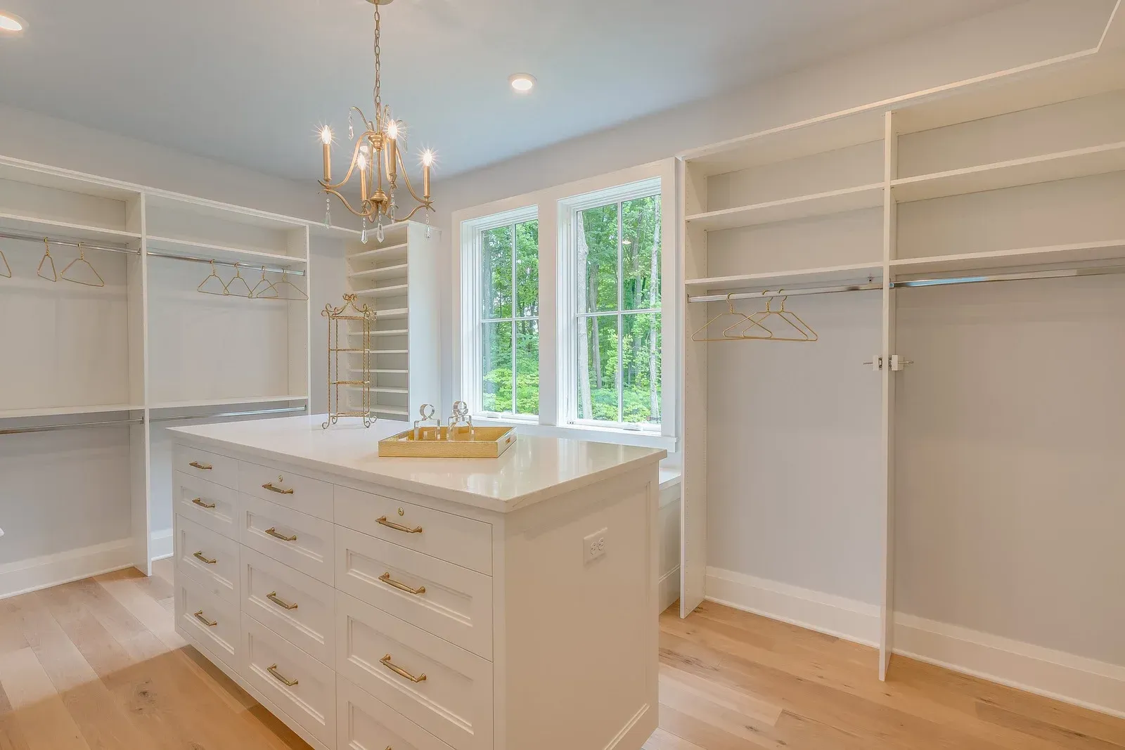 Walk-in closet with white cabinetry, wood floors, and a center island. A chandelier hangs over the island.