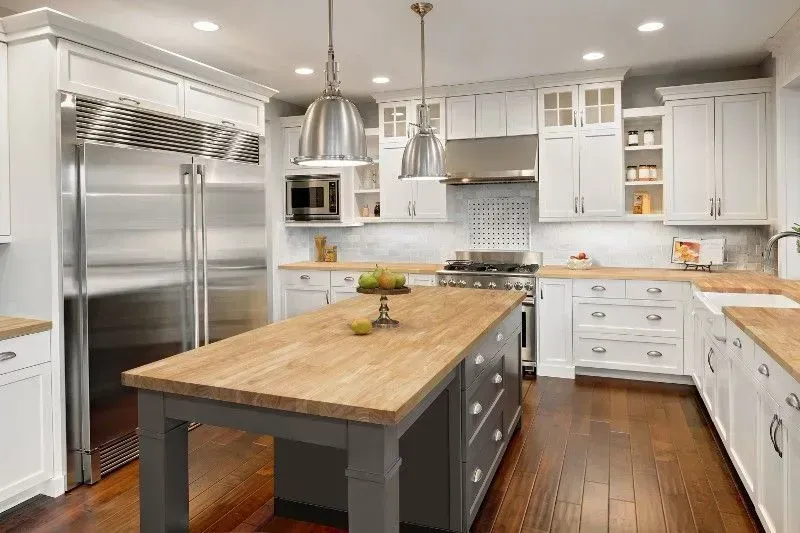 Bright white kitchen with stainless steel appliances, butcher block island, and dark wood floors.