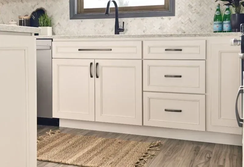 Cream-colored kitchen cabinets with black hardware and a beige rug in front.