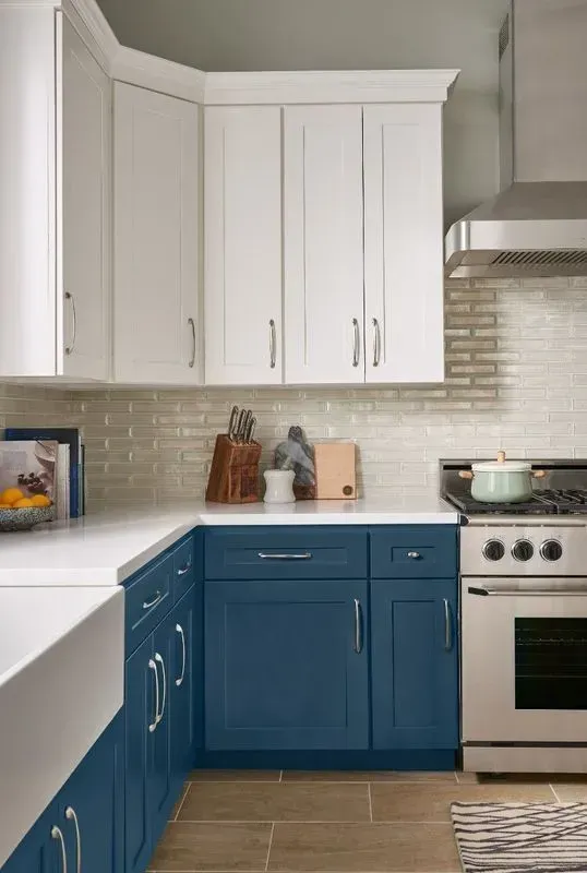 L-shaped kitchen with white upper and blue lower cabinets, stainless steel appliances, and a white countertop.