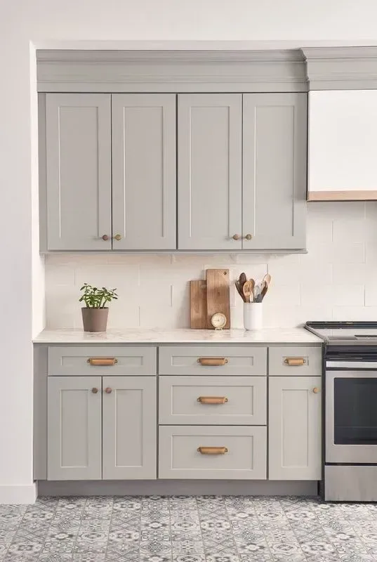 Gray kitchen cabinets with gold hardware and white countertops, a tiled backsplash, and a stainless steel stove.