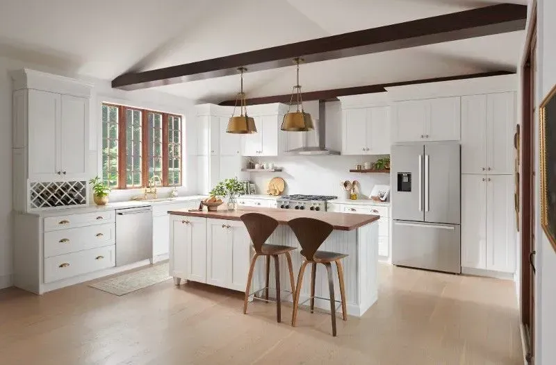 White kitchen with island, stainless steel appliances, wood accents, and brass lighting.