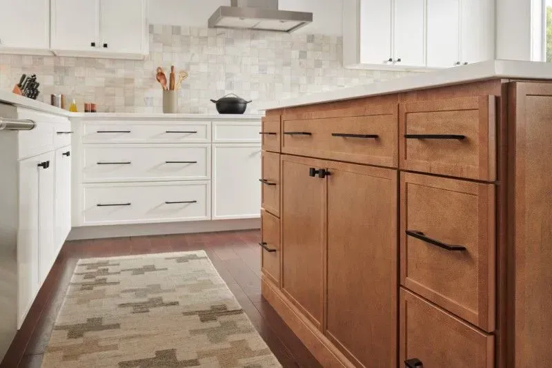 Kitchen with light cabinets, wood island, patterned rug, and dark hardware.