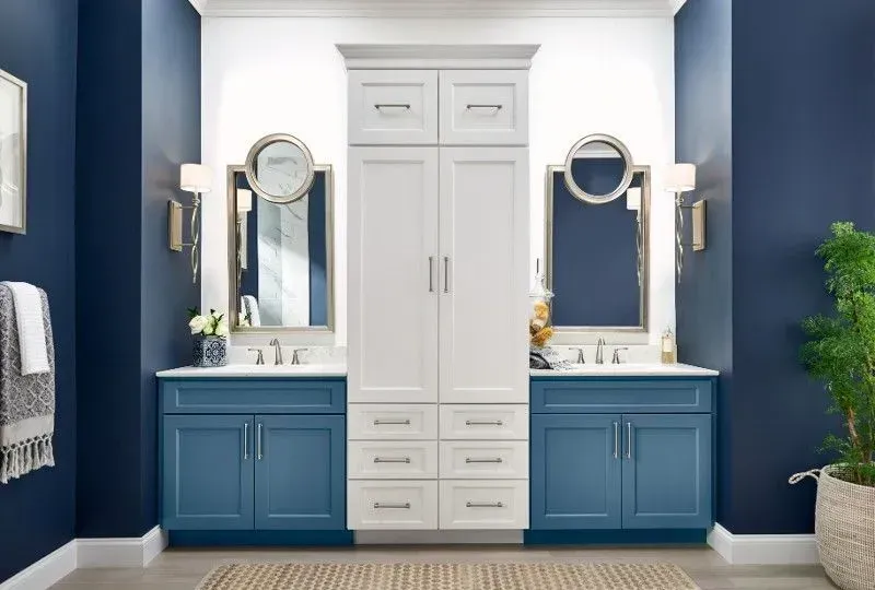 Bathroom with blue and white cabinets, mirrors, and a tall storage unit on a dark blue wall.