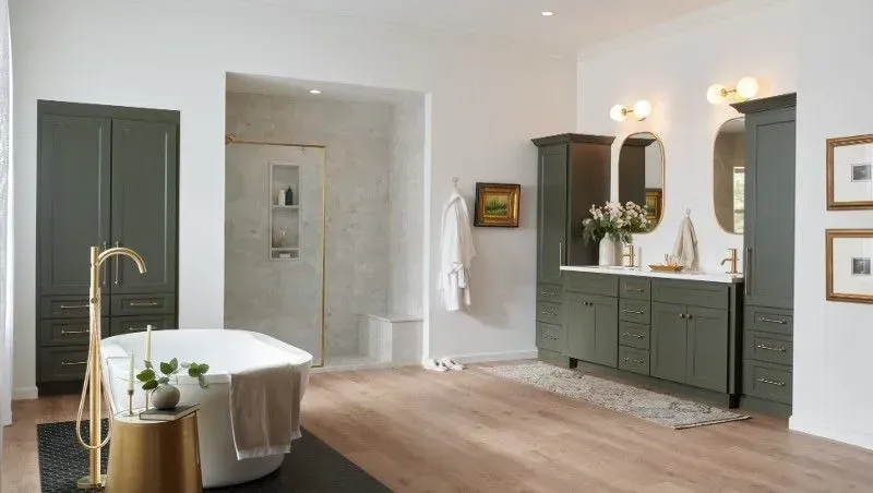 Spacious bathroom with green cabinets, white bathtub, and wooden floor.