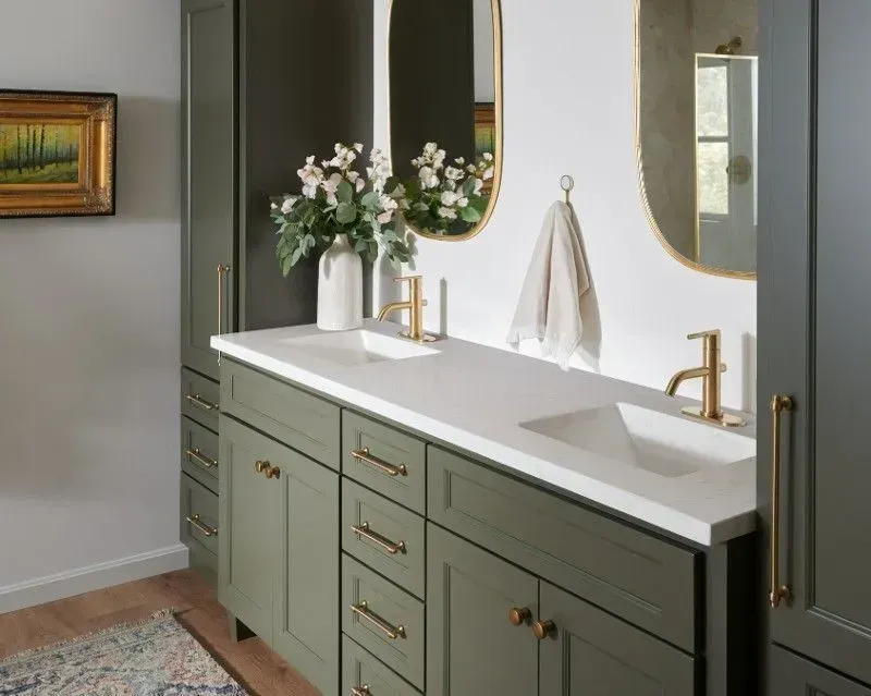 Green bathroom vanity with white countertop, gold fixtures, and two oval mirrors.