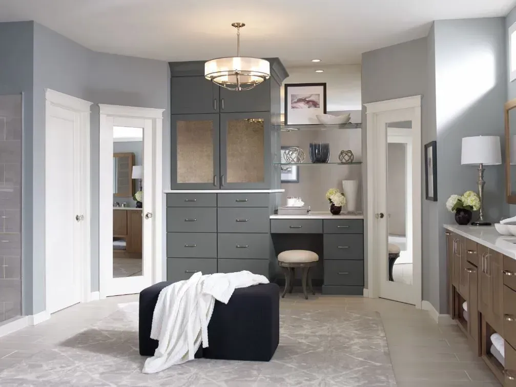 Gray and white walk-in closet with dark gray built-ins, an ottoman with a white throw, and an overhead light.