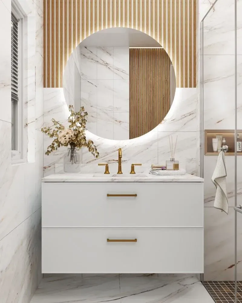 Modern bathroom with white marble tile, floating white vanity, gold fixtures, and a round illuminated mirror.