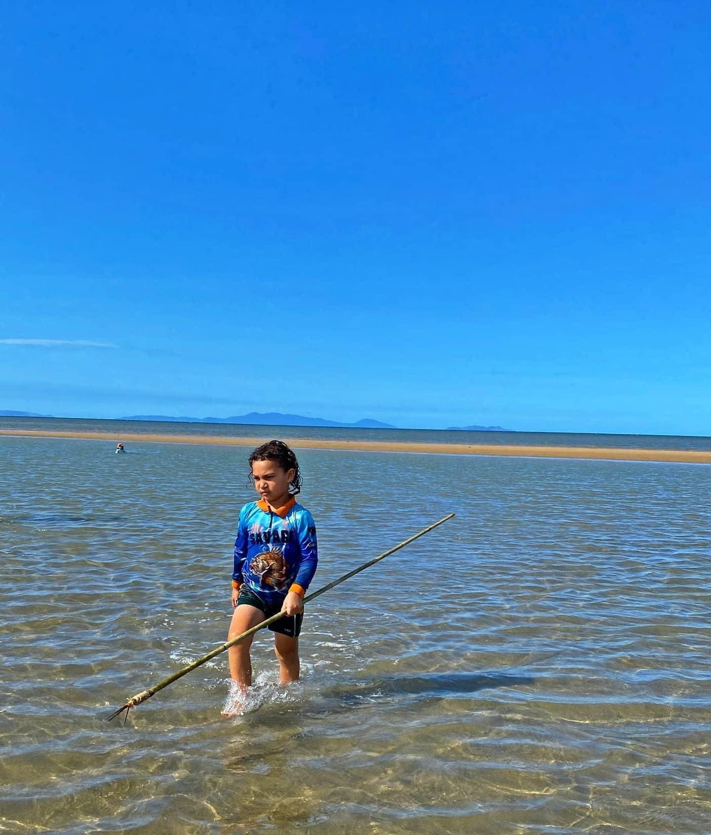 A young boy is standing in the water holding a stick.