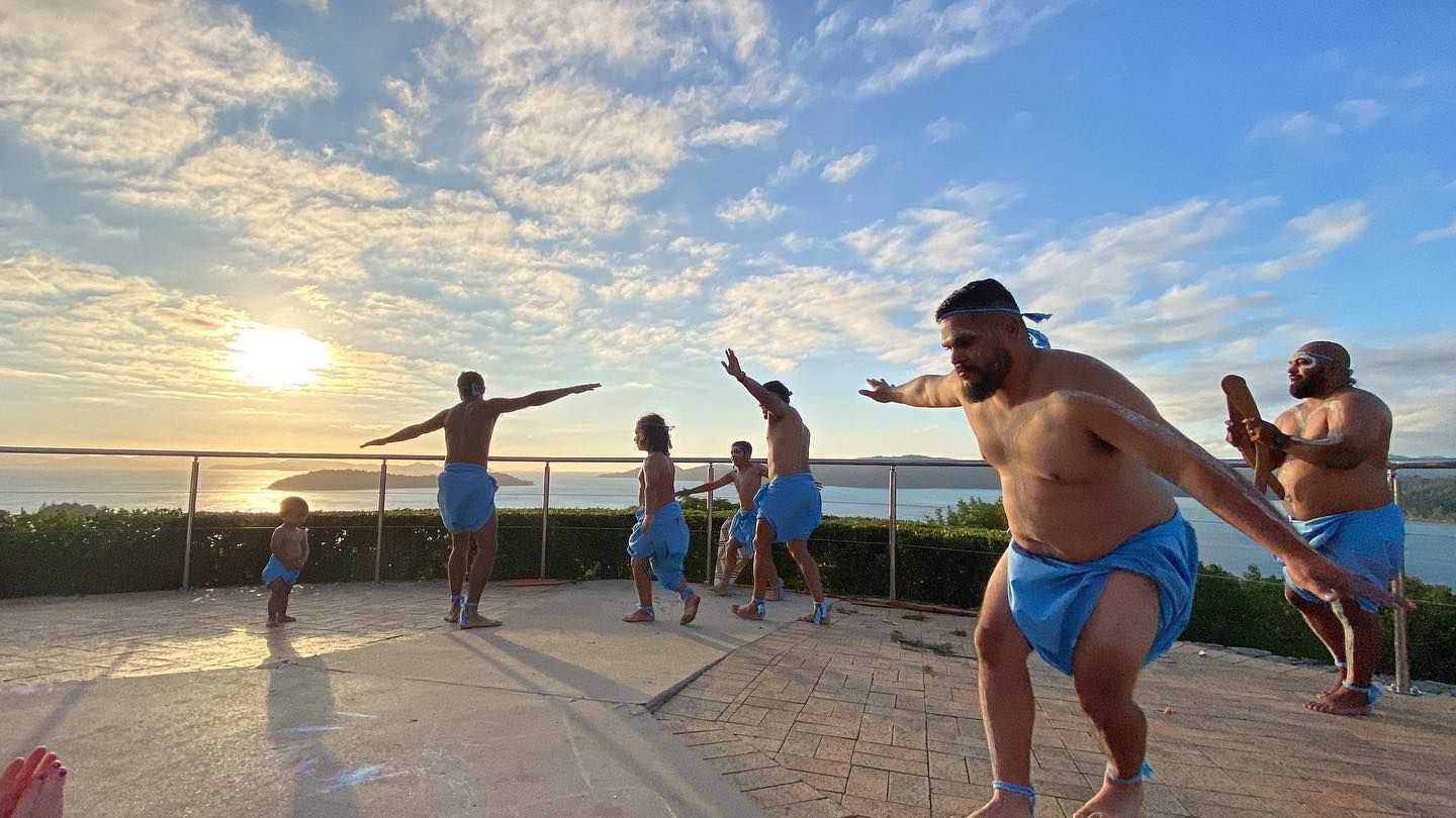 A group of men are dancing on a beach at sunset.