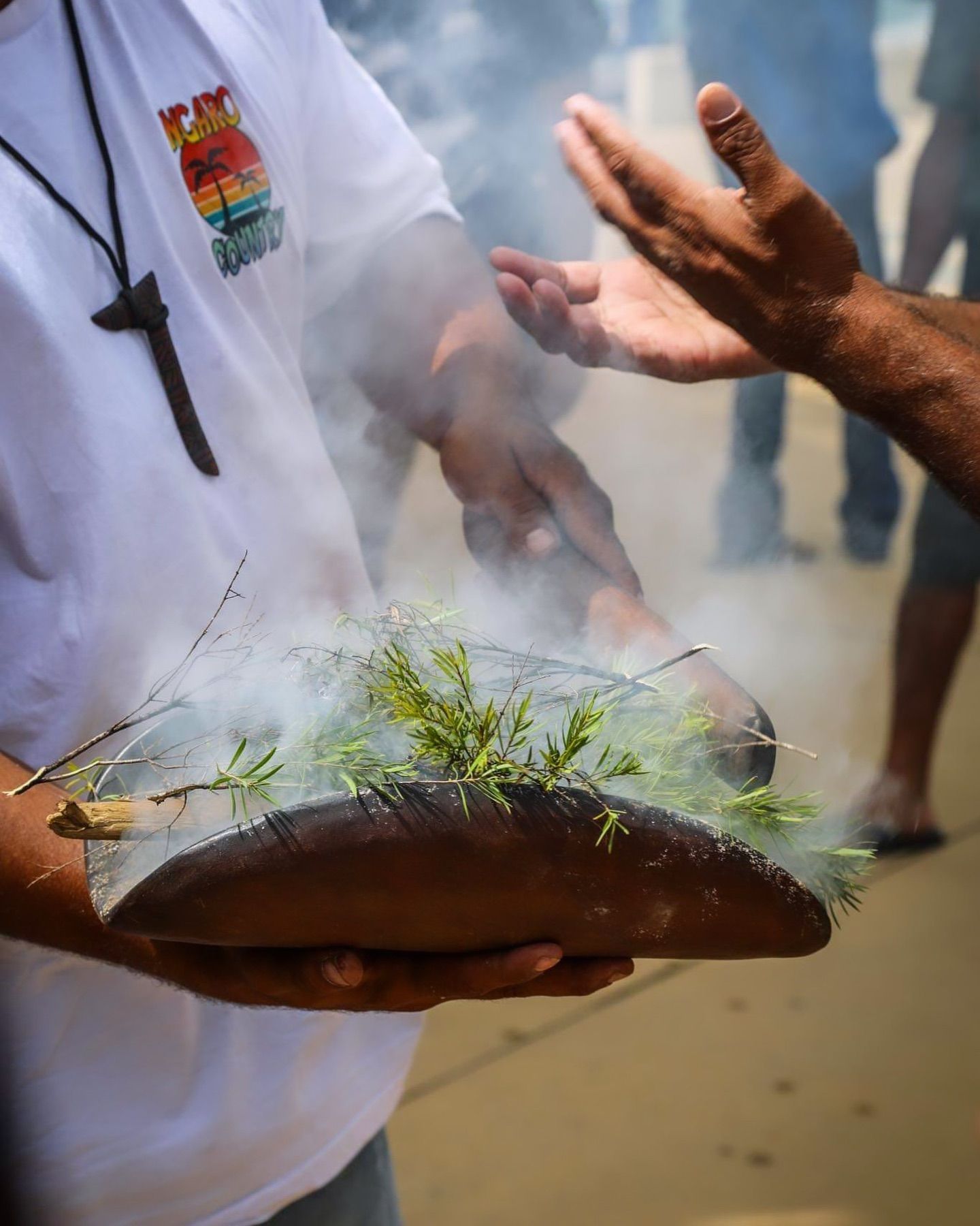 A man in a white shirt is holding a piece of wood with smoke coming out of it.