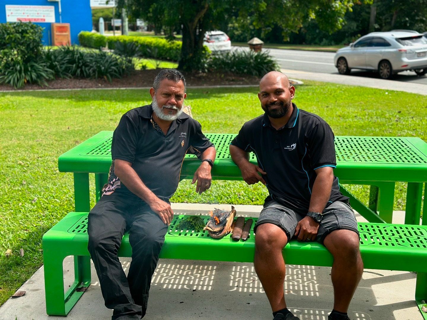 Two men are sitting on a green picnic table.