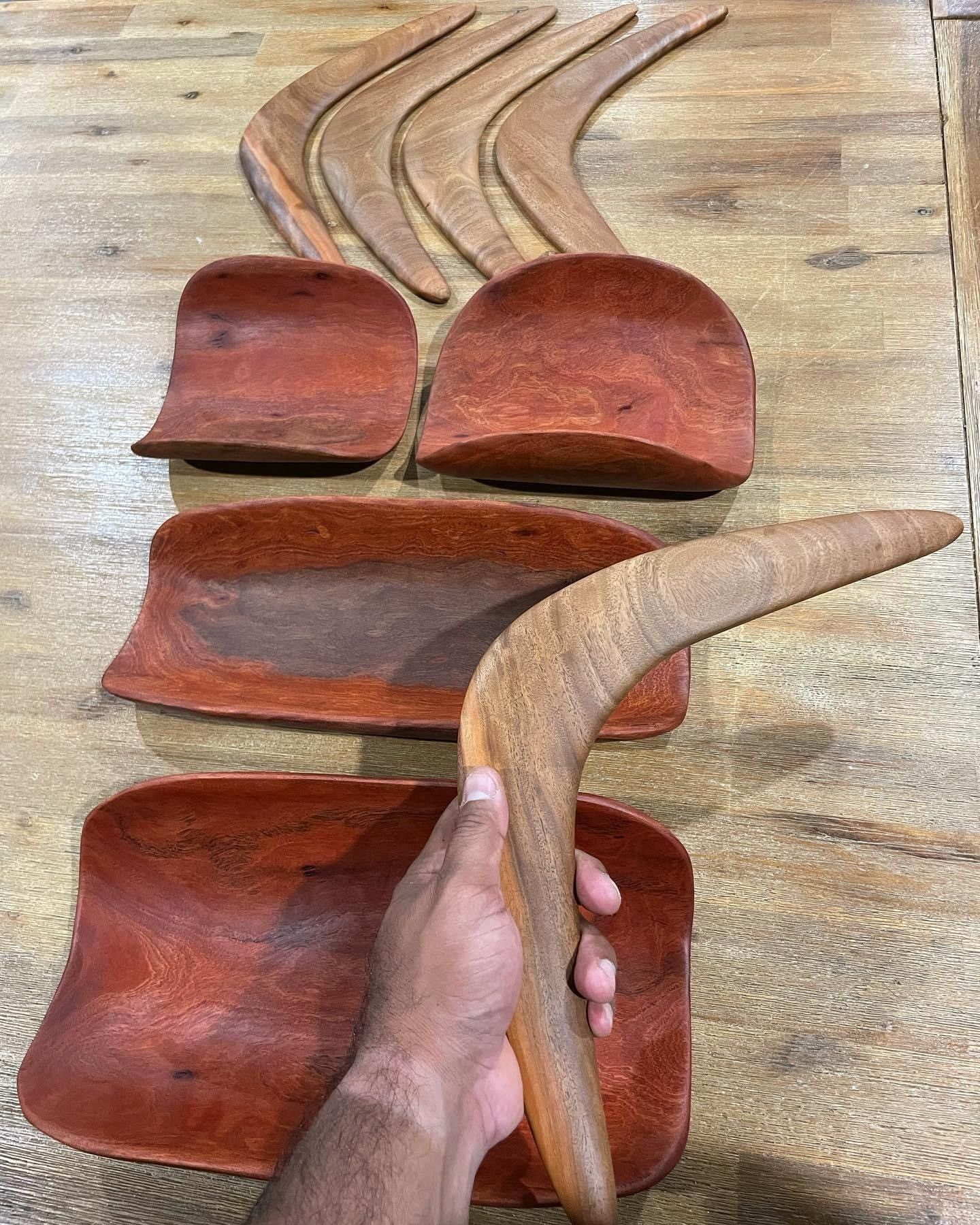 A person is holding a wooden boomerang in front of a wooden table.