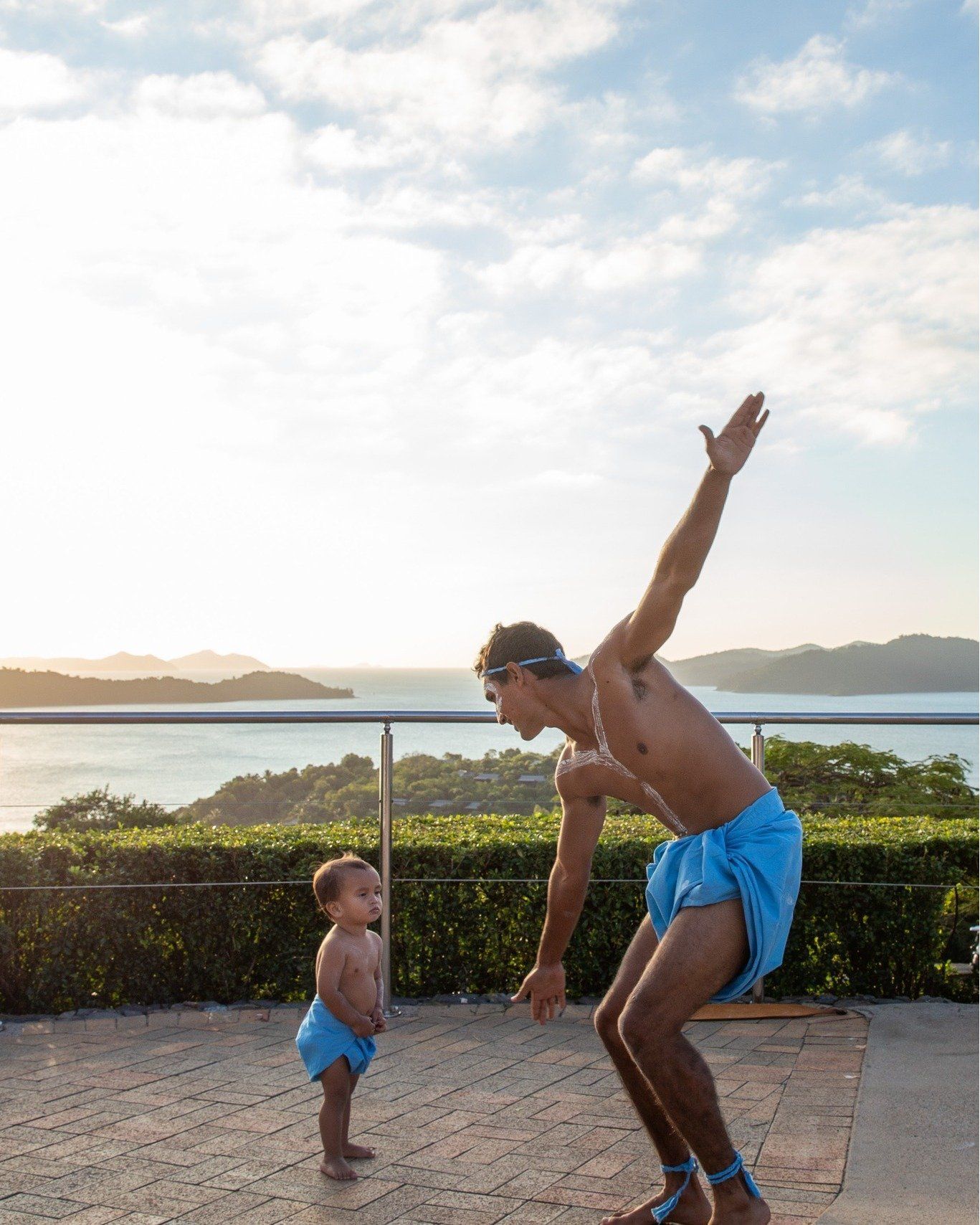 A man and a baby are playing on a balcony overlooking the ocean.