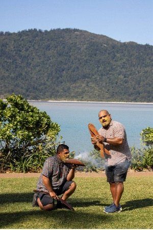 Two men are kneeling on the grass in front of a body of water.