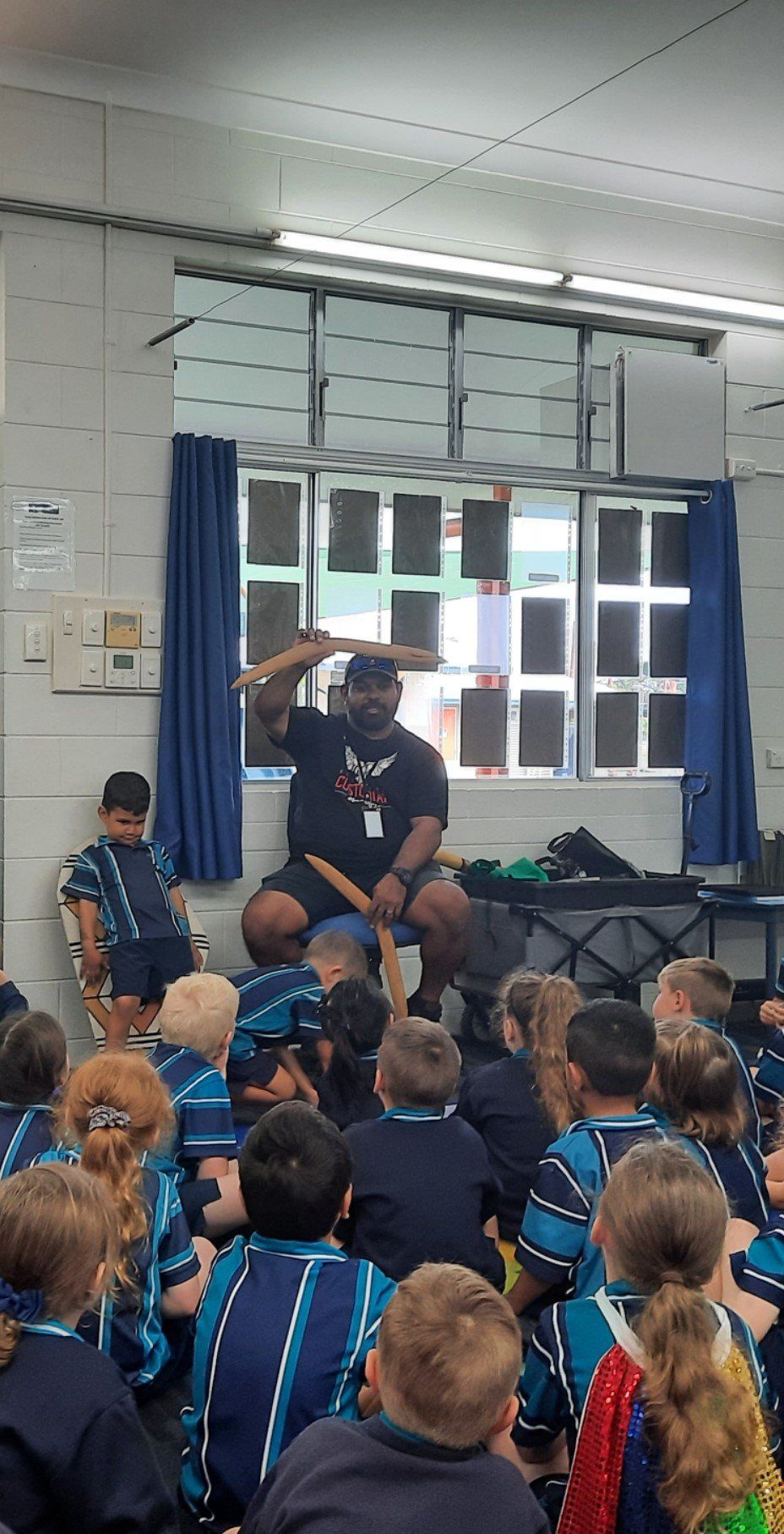 A man is sitting in front of a group of children in a room.