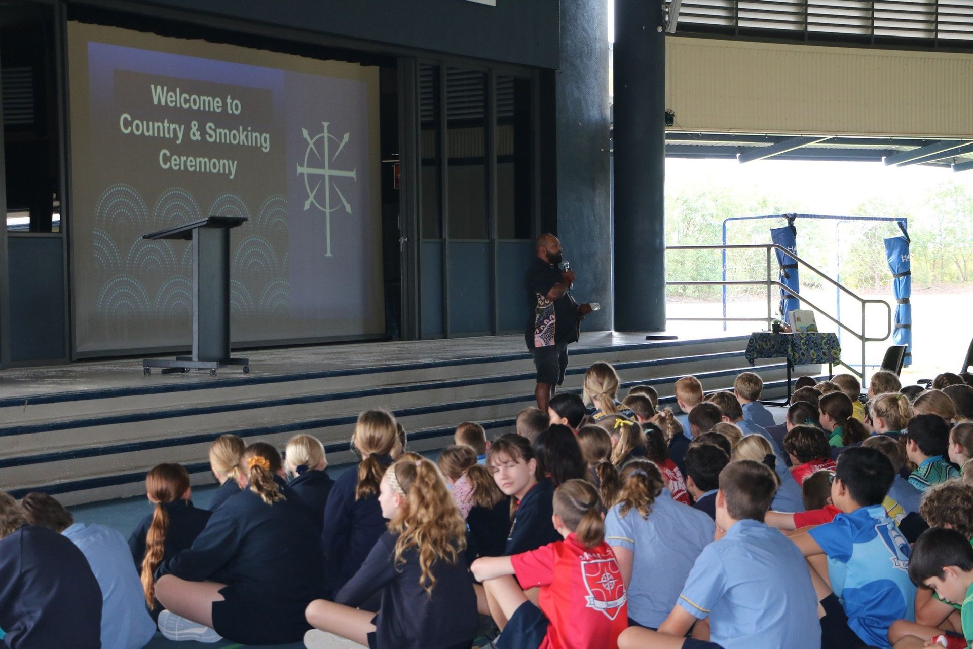 A group of children are sitting in front of a screen that says welcome to country & speaking ceremony