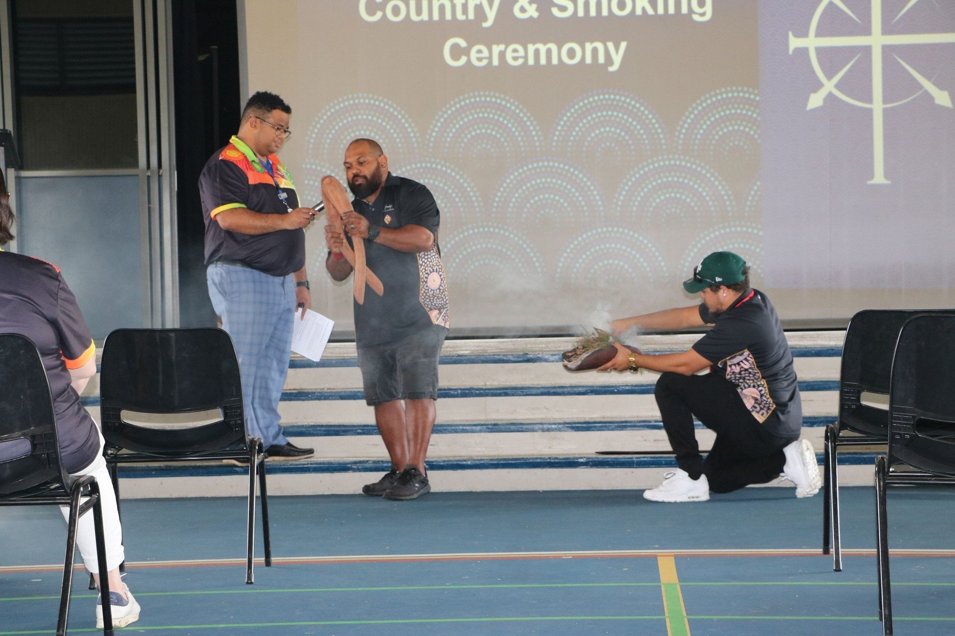 A man is kneeling down in front of a group of people at a ceremony.