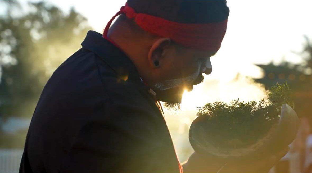 A man wearing a red headband is holding a plant in his hands.
