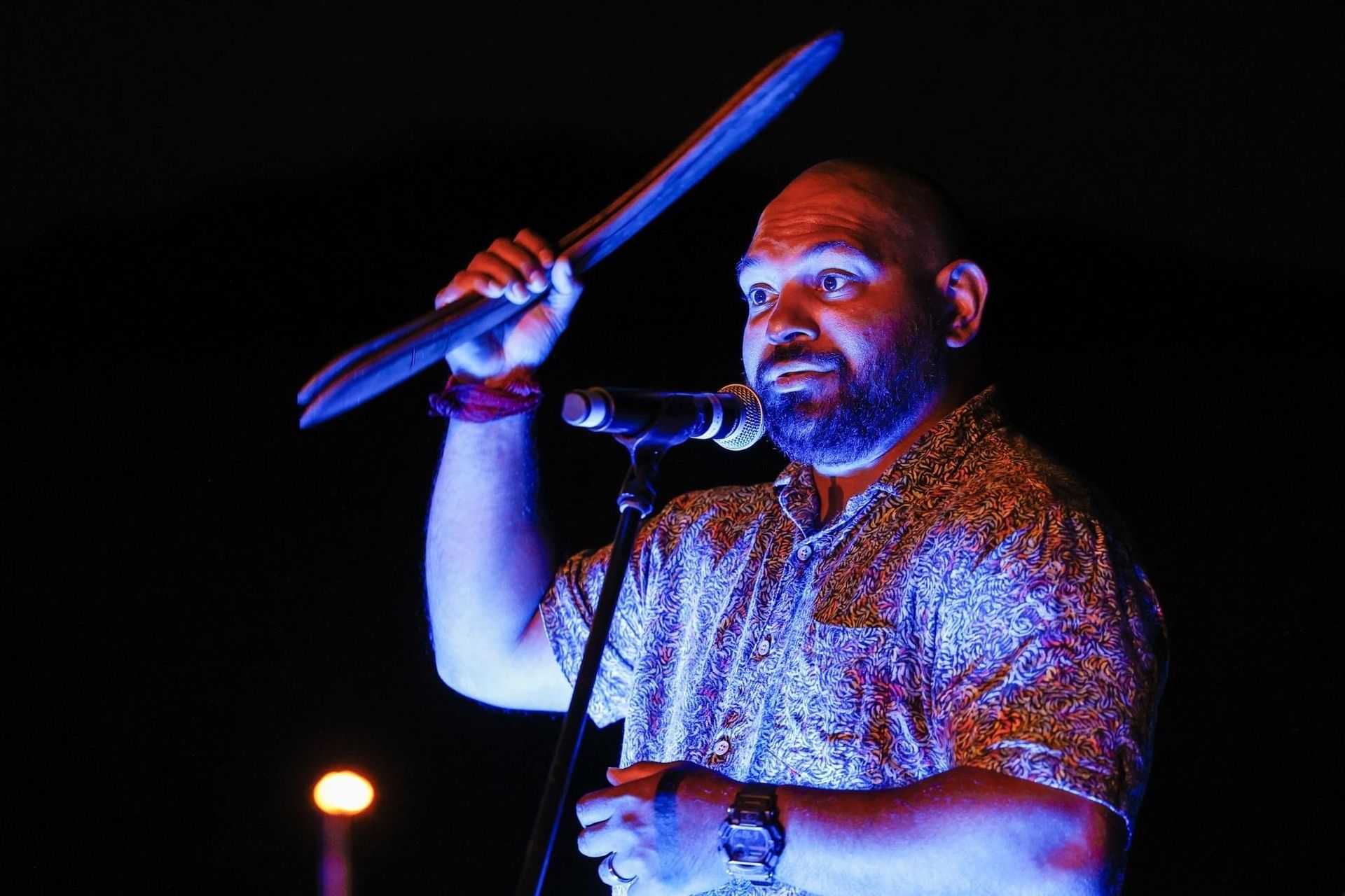 A man with a beard is singing into a microphone while holding a stick.