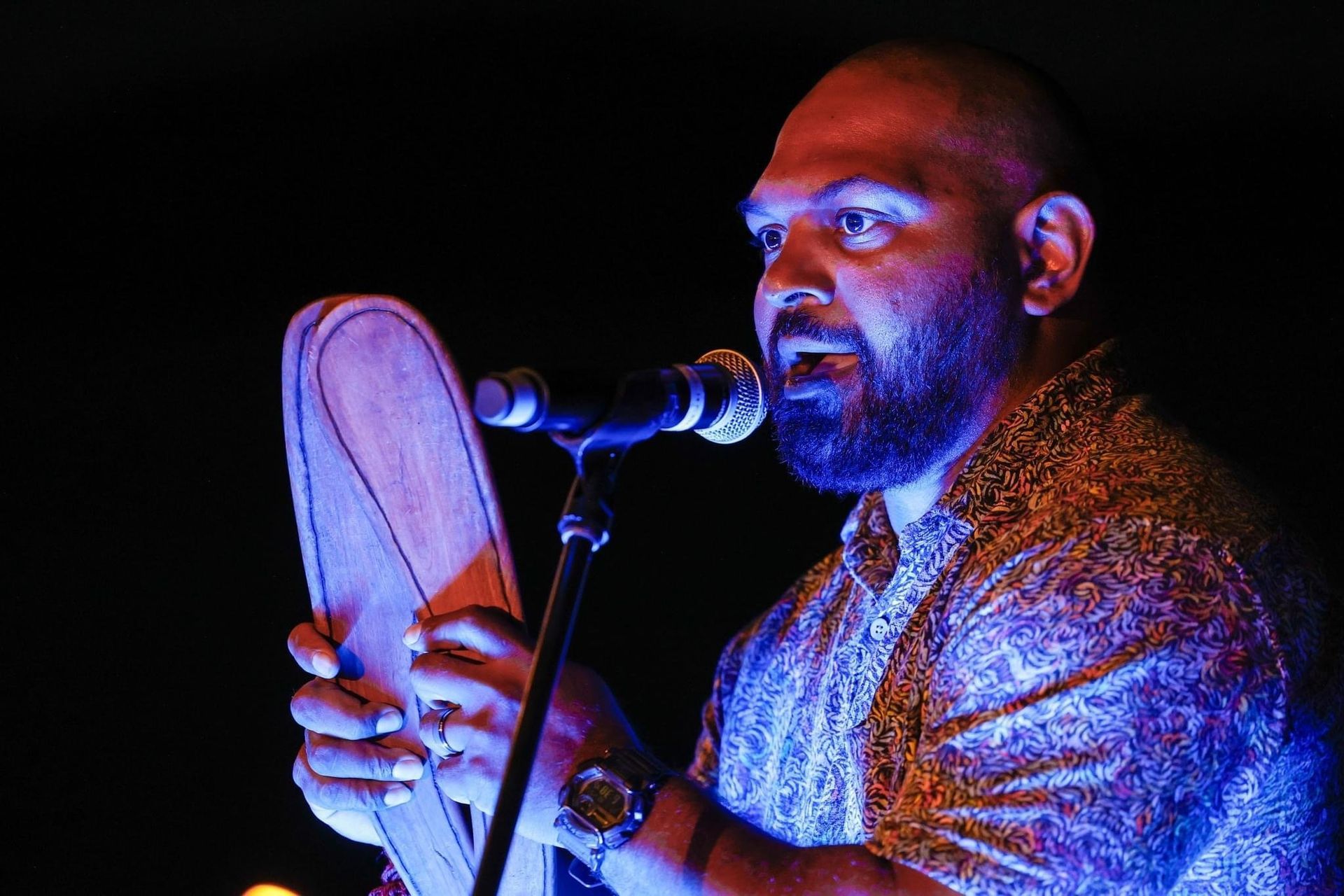 A man with a beard is singing into a microphone while holding a shoe.