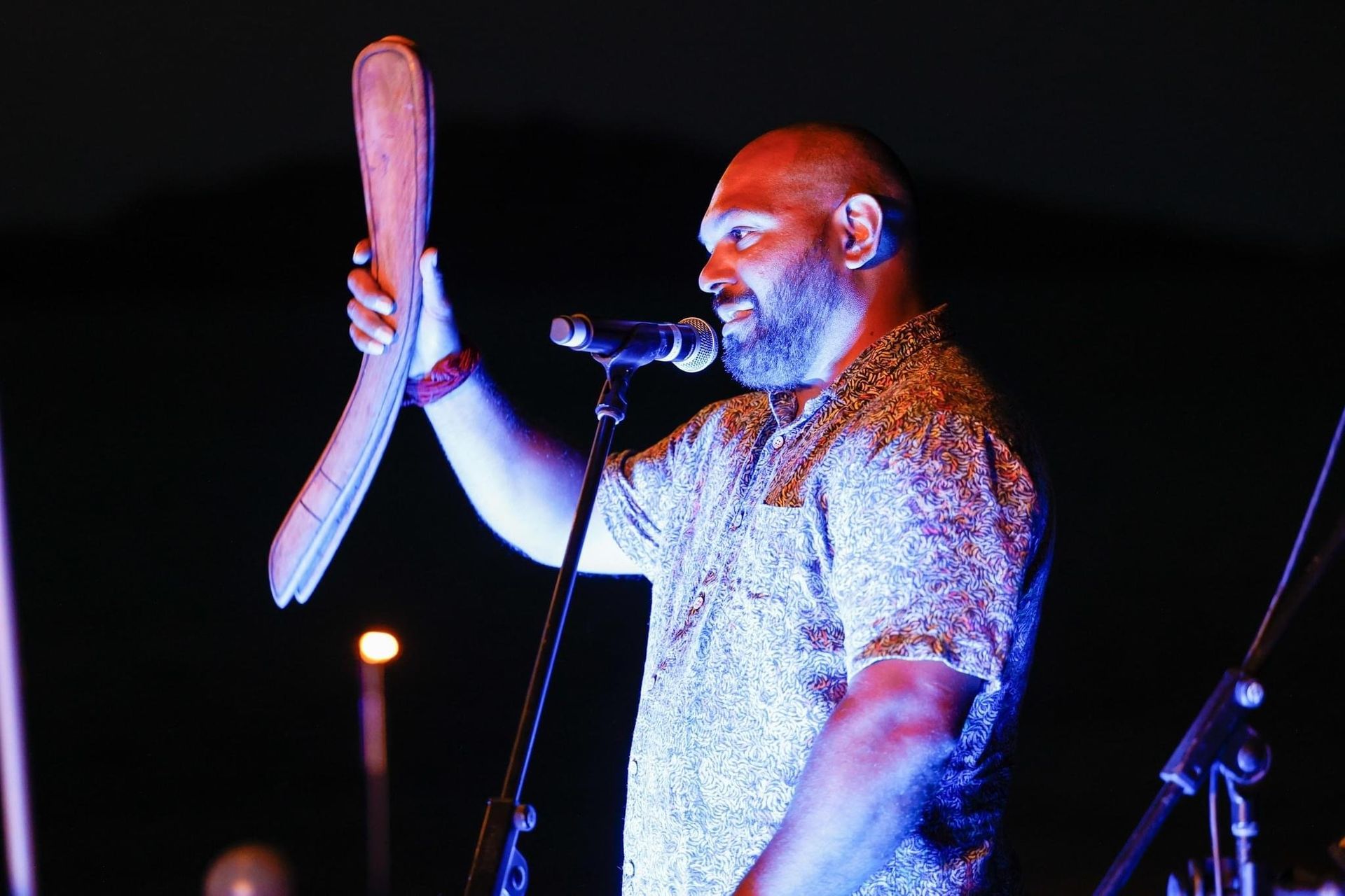 A man is singing into a microphone while holding a wooden stick.
