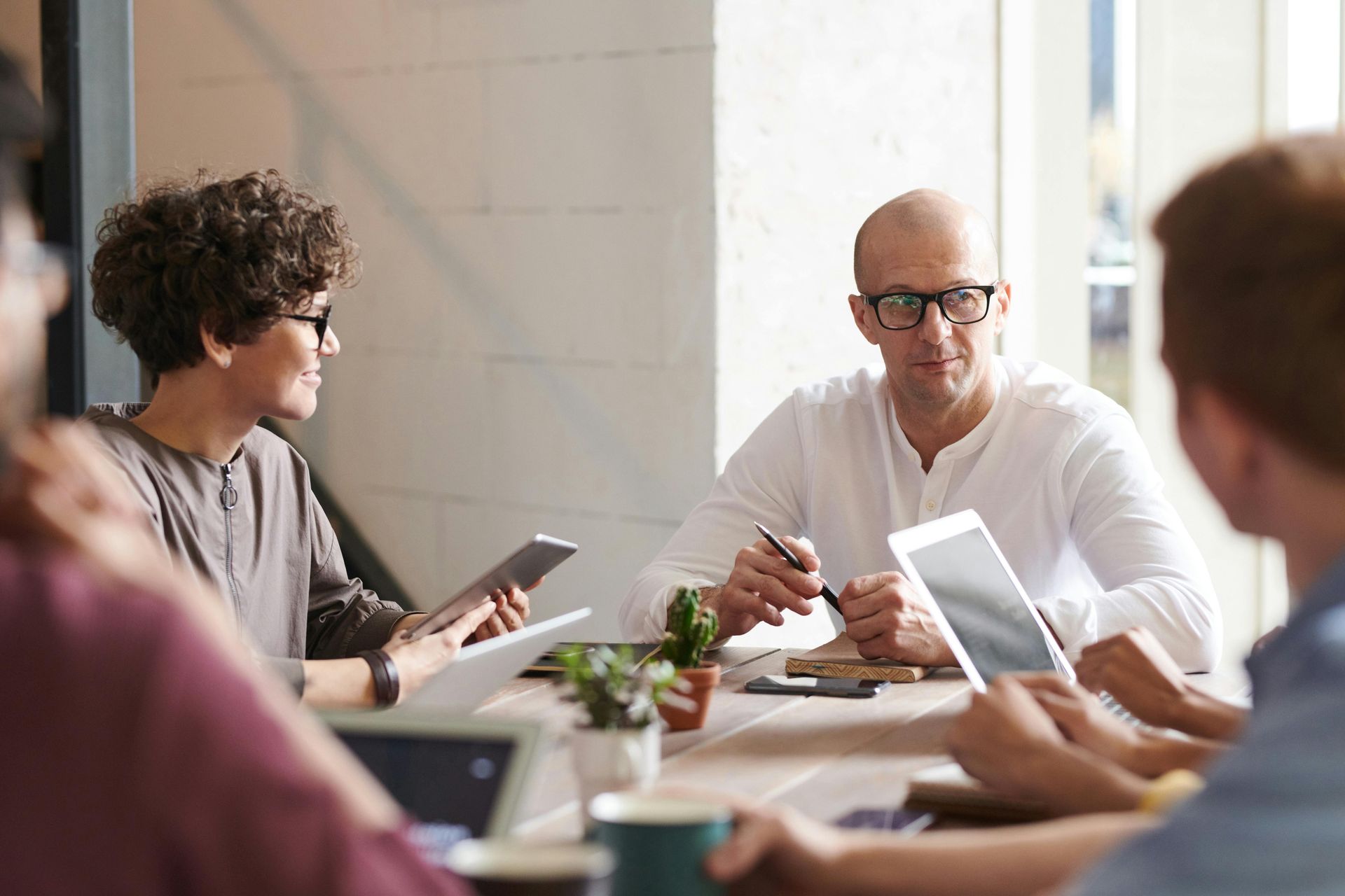 People gathered around a table in a bright office meeting, using tablets and discussing work.