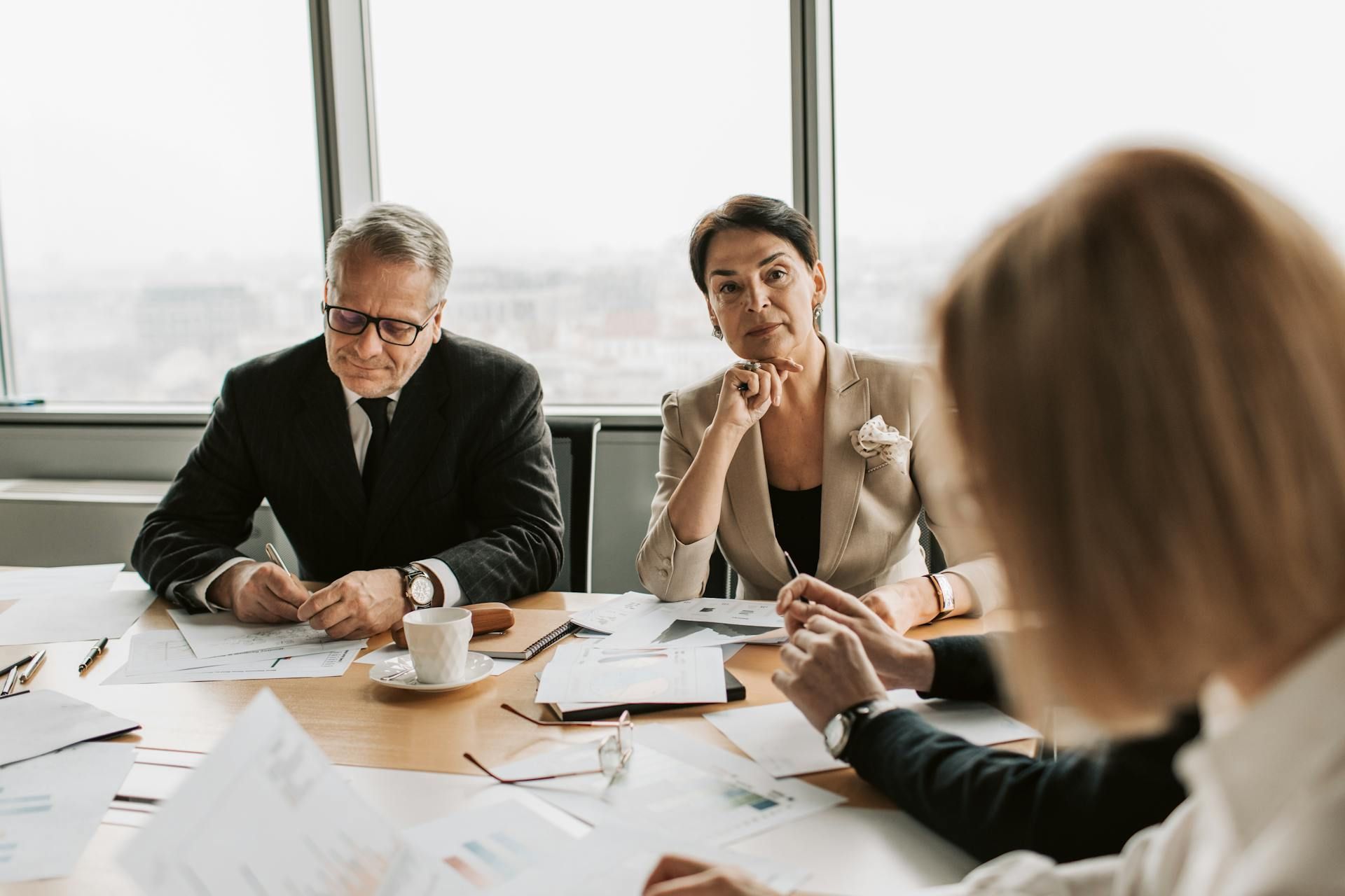 Business meeting around a table with documents, coffee cups, and a laptop in a bright office