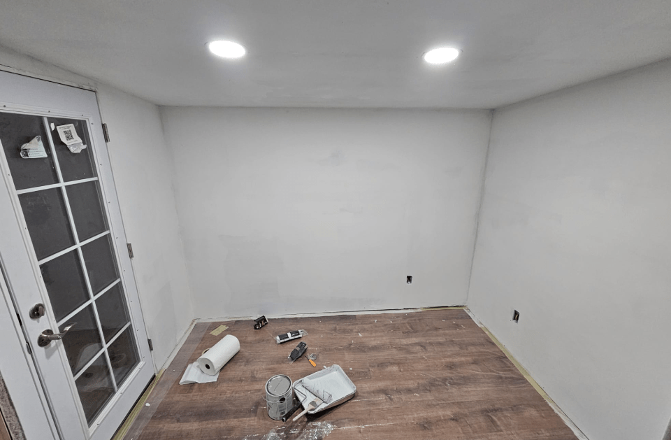 A small room with new wood flooring, white walls, and a door on the left side; construction tools in the center.