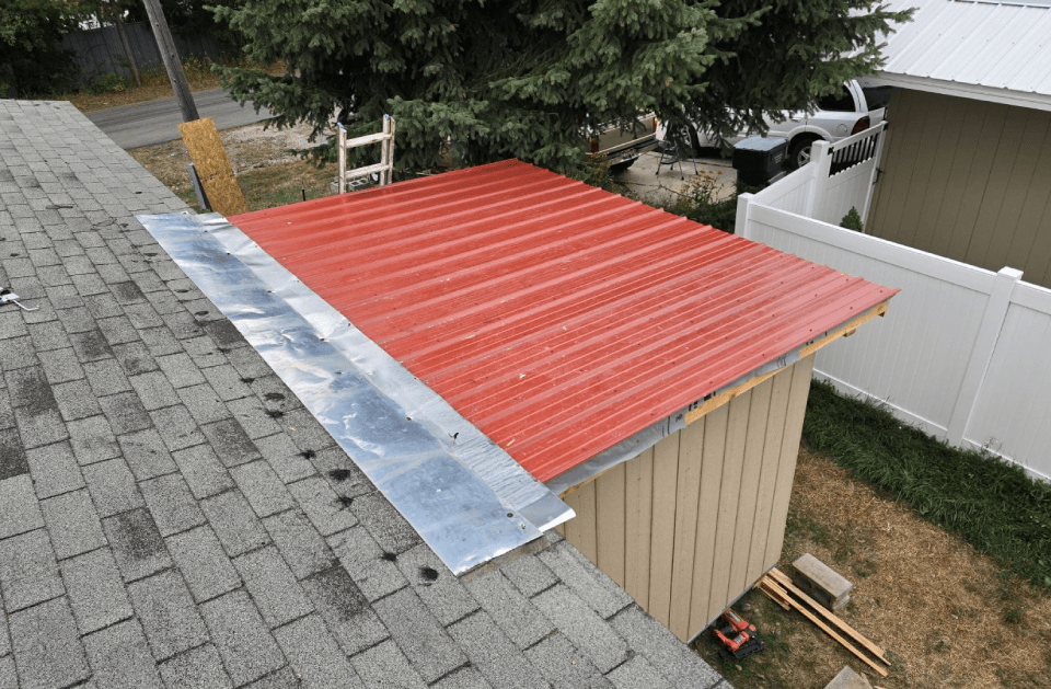 Red metal roof installed next to a gray shingle roof on a small building; close-up view.