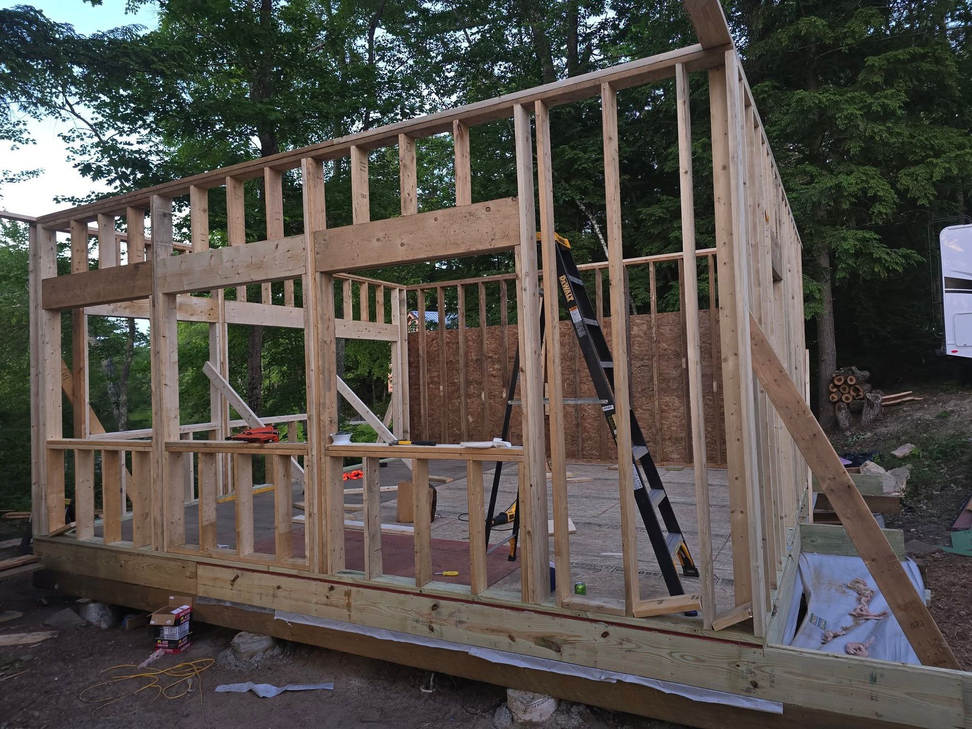 Wooden frame of a small building under construction, exterior view with ladder.