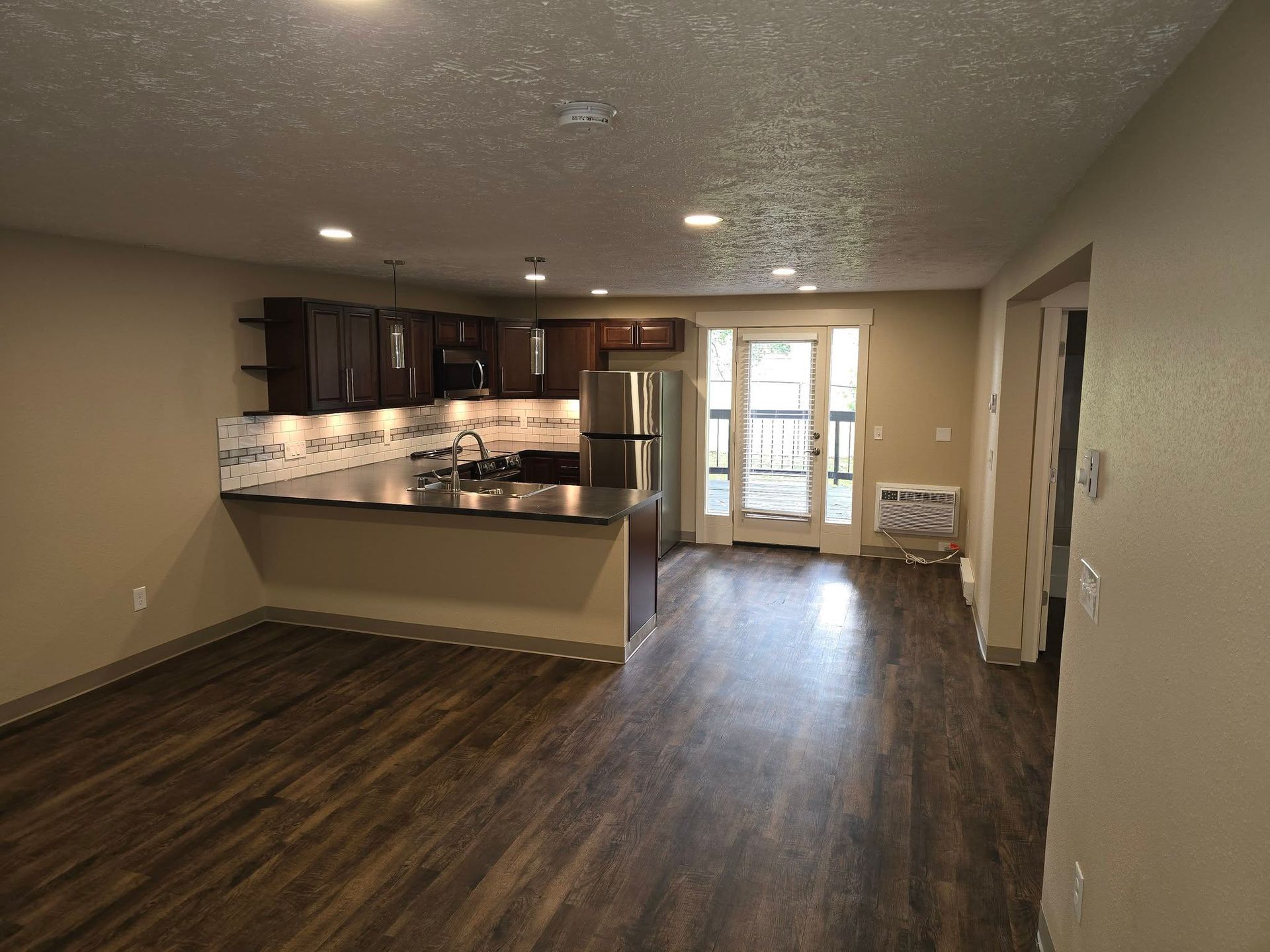 Interior view of an open-concept living space with kitchen, dark wood cabinets, and hardwood floors.