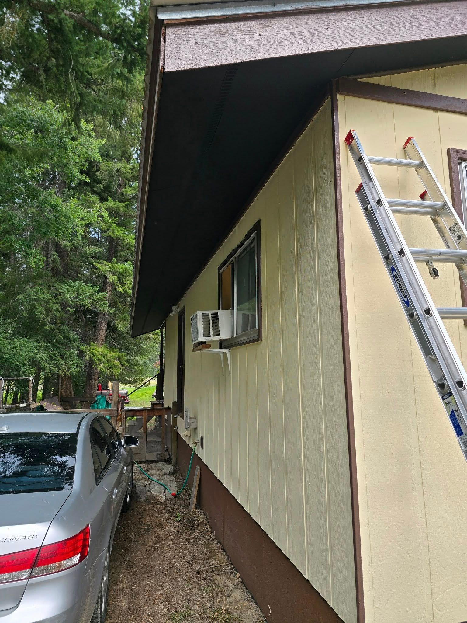 Side view of a house with a ladder propped against the wall; a car is parked next to the house.