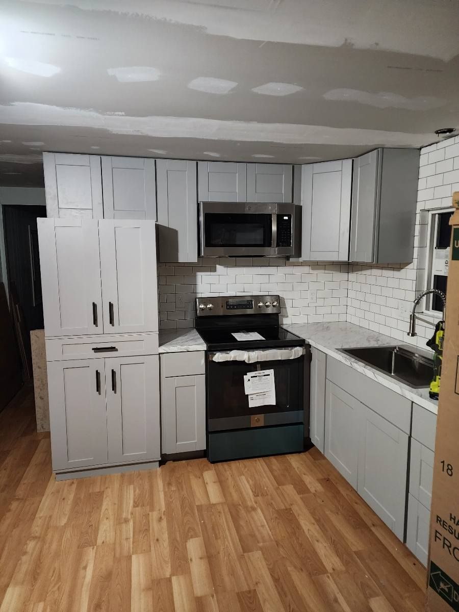 Newly renovated kitchen with gray cabinets, a black stove, and a white brick-like backsplash.
