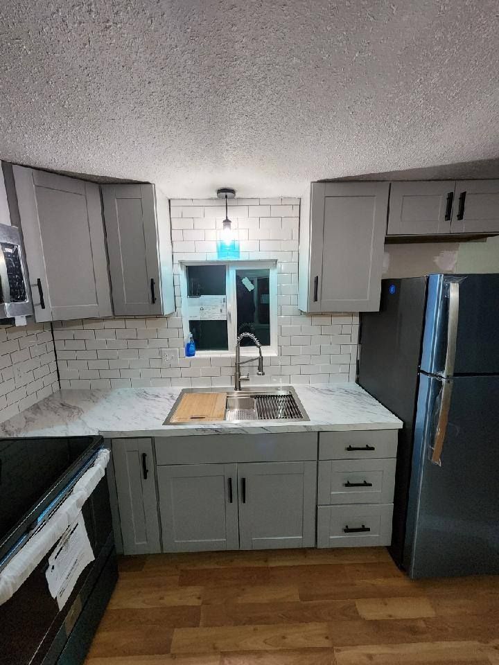 Gray kitchen cabinets with white countertops and a black refrigerator.