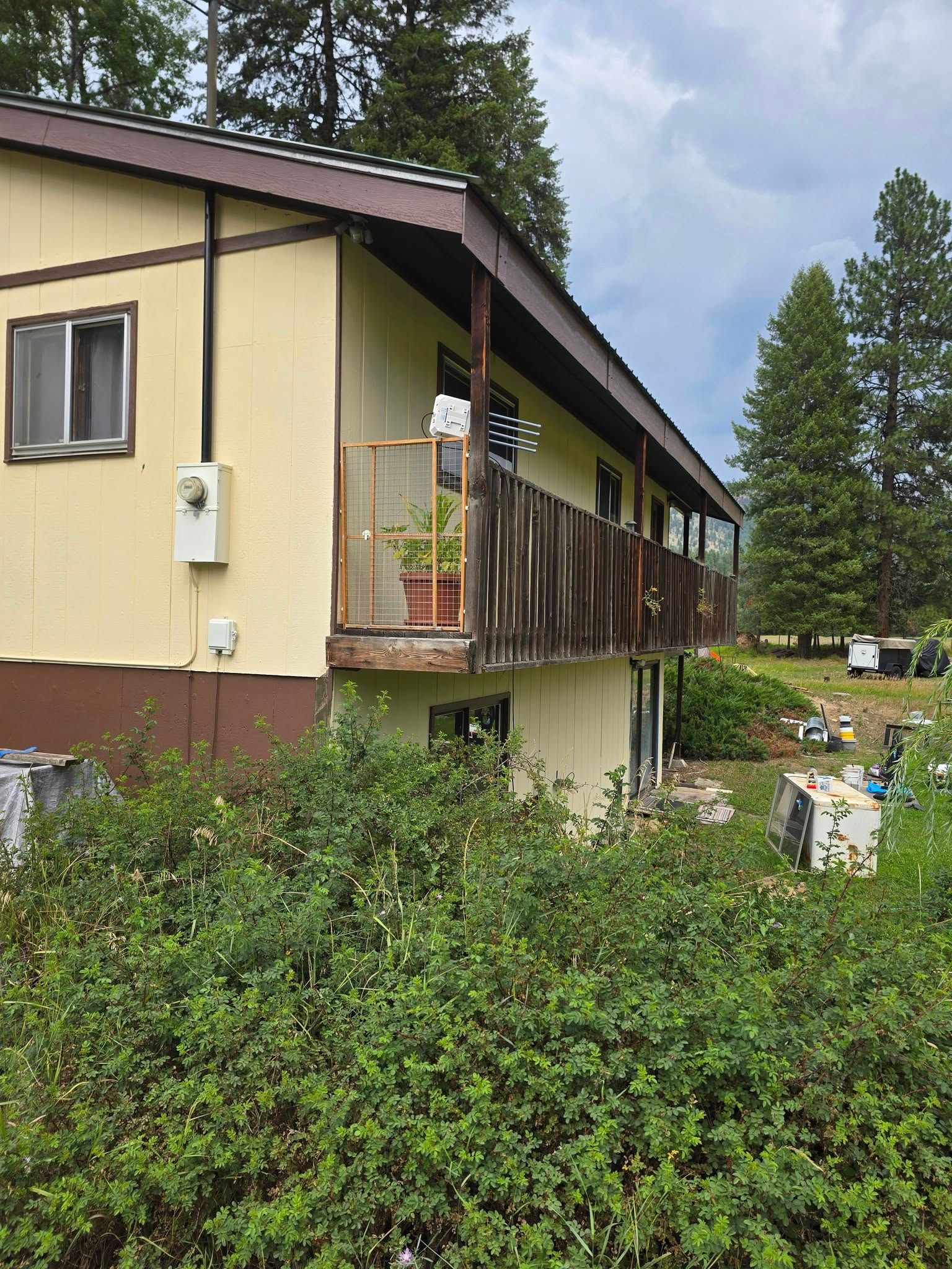 Beige house with brown trim and balcony; overgrown bushes in front.