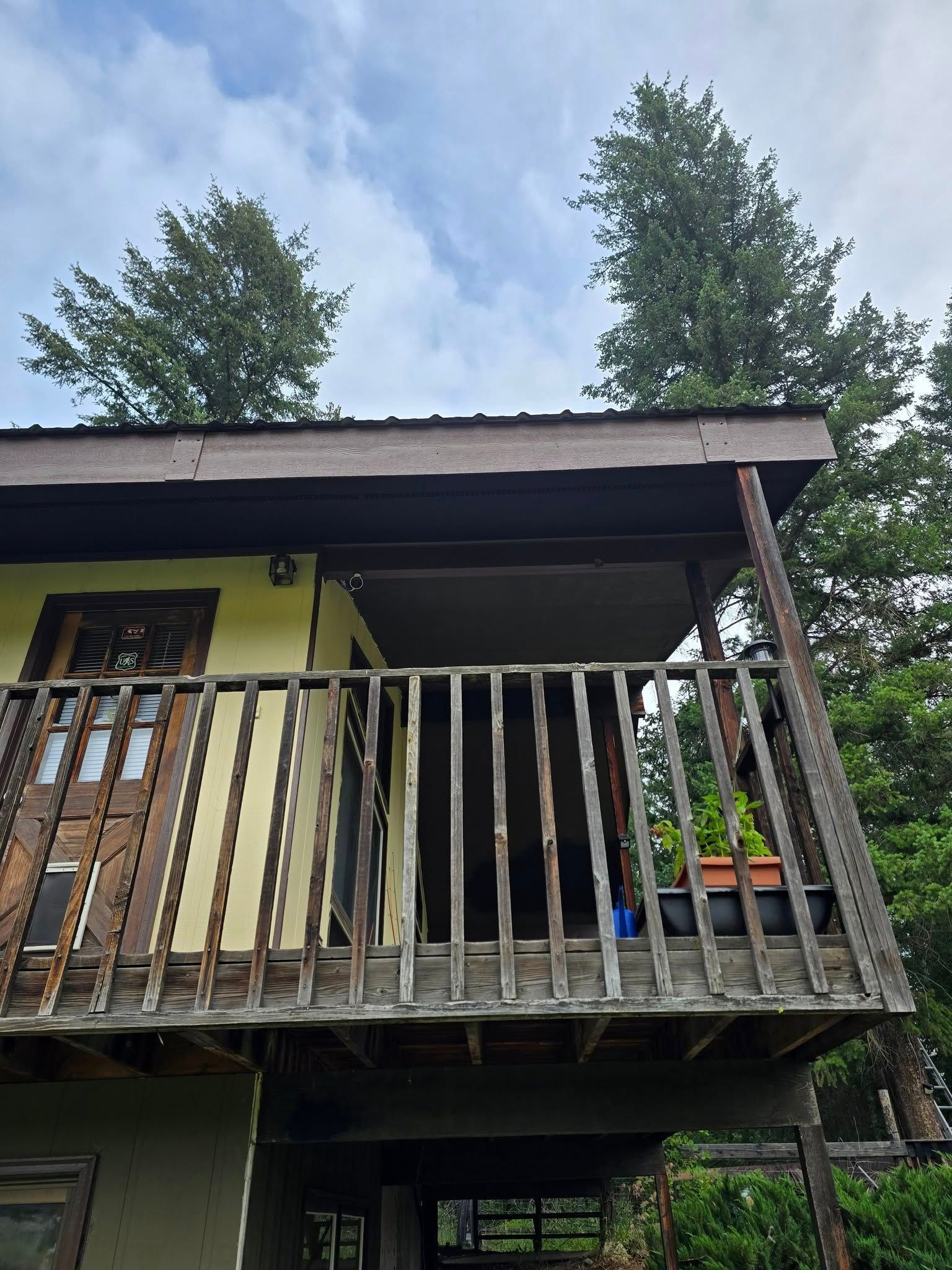 Wooden balcony on a yellow building under a cloudy sky, with trees visible in the background.