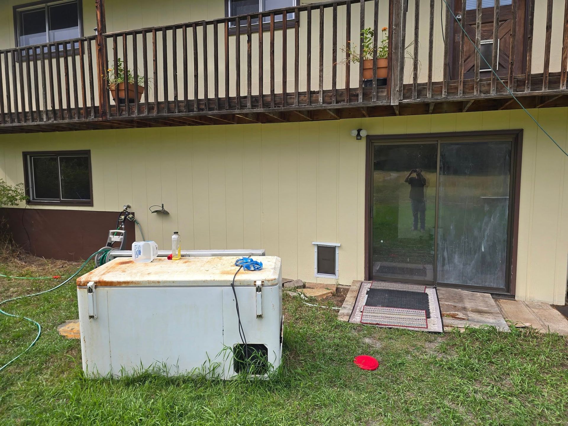 Backyard view of a house with a deck, sliding glass door, and a weathered freezer.