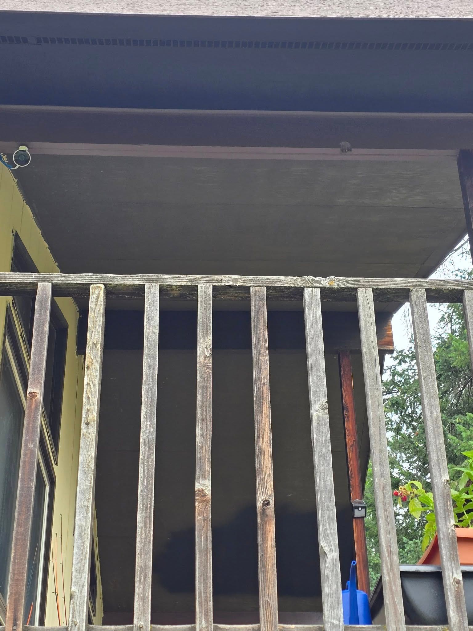 Wooden balcony railing with a partially obscured view; tan wall visible, along with a blue object.