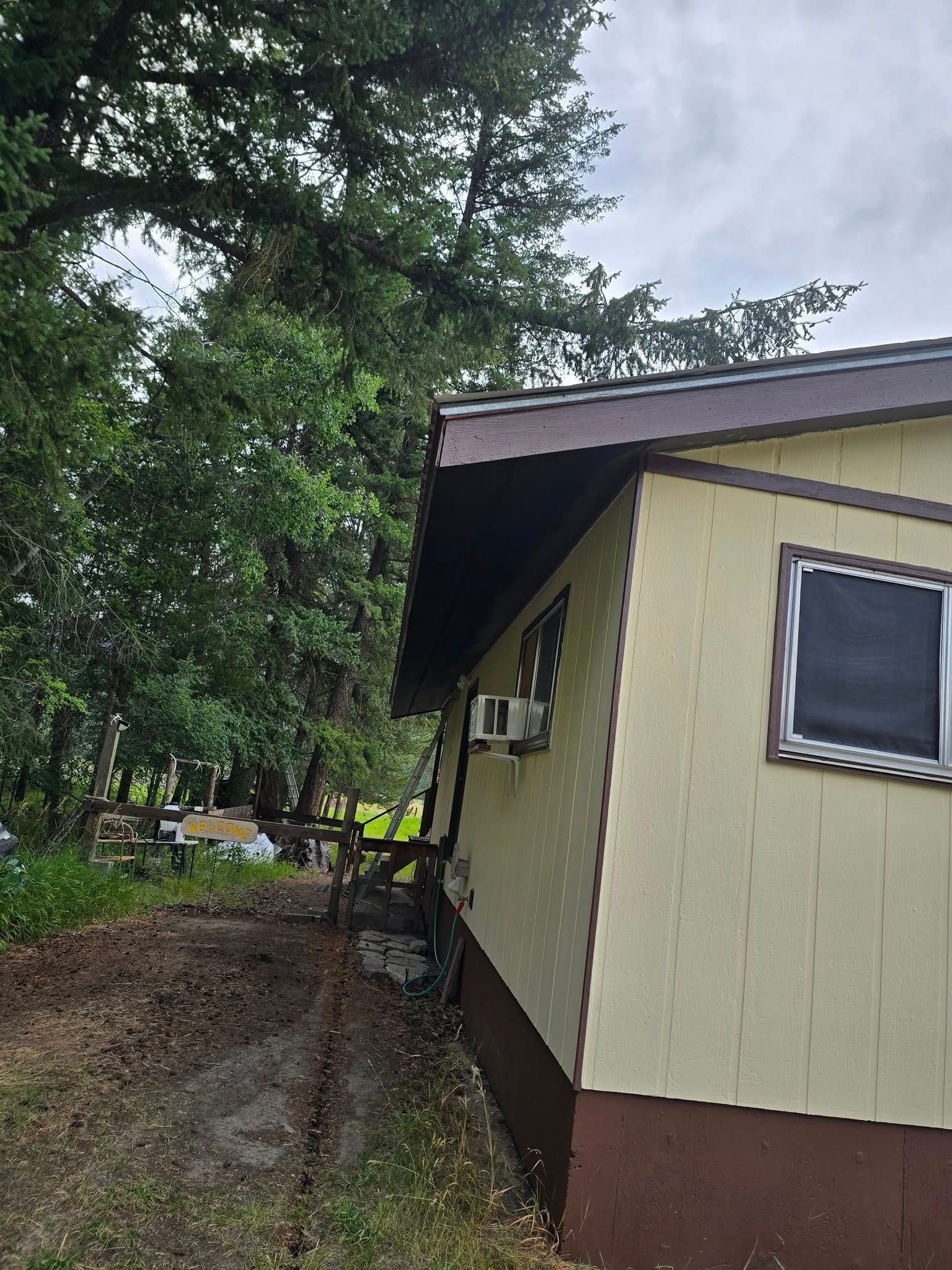 Tan building with dark brown trim, next to a tree and a walkway. Cloudy sky.