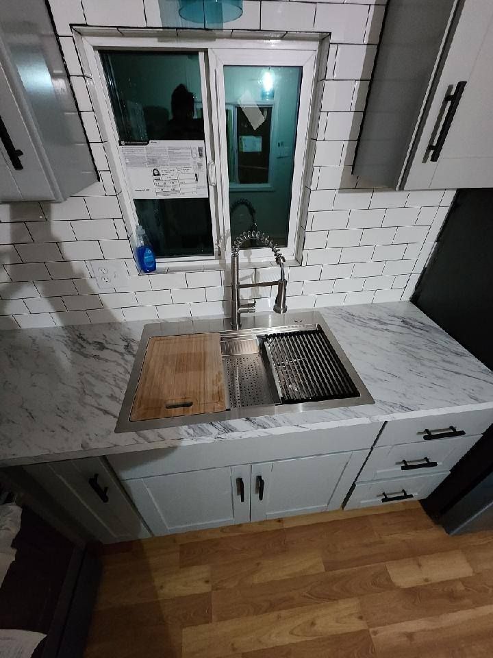 Kitchen sink with a marble countertop, white cabinets, and a window above.