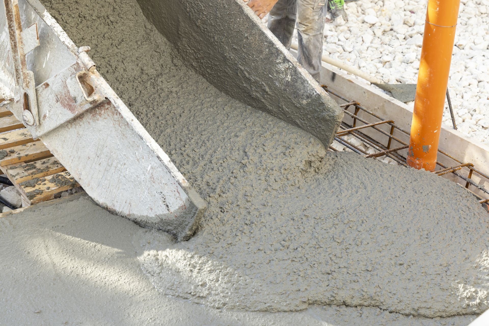 Fresh concrete flows from a chute onto a reinforced surface at a construction site.