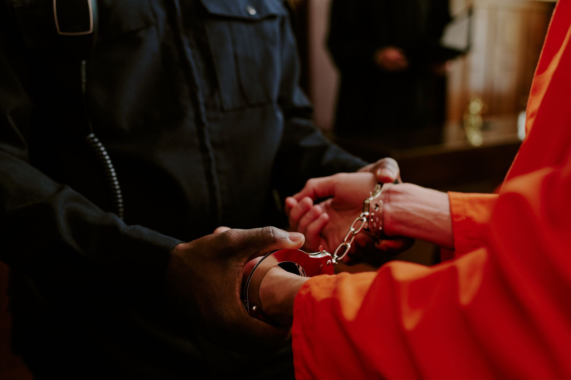 An inmate is being detained by the hands by a police officer, inside a room An inmate is being detained by the hands by a police officer, inside a room