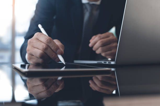 Crop view of a businessman in a black suit, performing an inmate search on a tablet and a laptop.