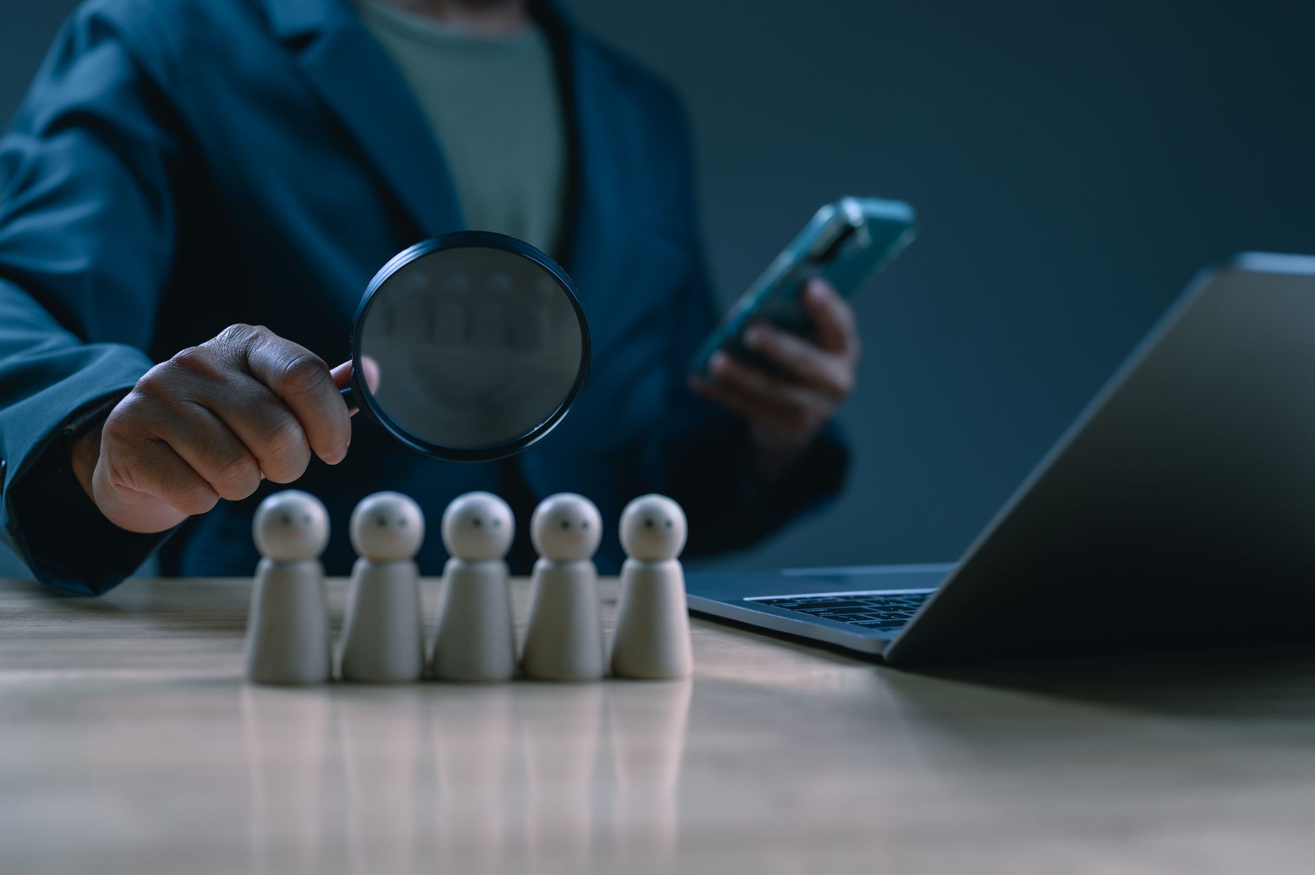 A person holding a magnifying glass, examining wooden figures, showcasing inmate research.