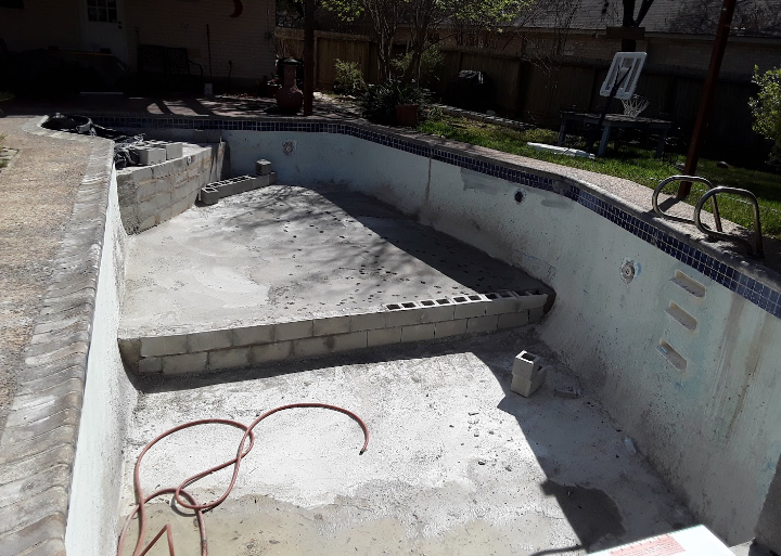 An empty swimming pool with a hose laying on the ground.